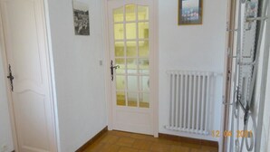 Un pasillo con una puerta blanca, una puerta de vidrio con un tono amarillo y un radiador en la pared.