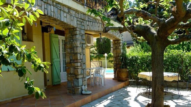 Un edificio de piedra con un patio adoquinado, mobiliario exterior y un árbol.