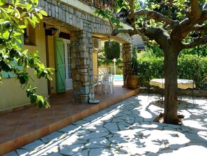 Un edificio de piedra con un patio adoquinado, mobiliario exterior y un árbol.