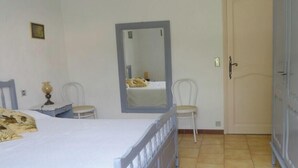 Un dormitorio con cama, una silla, armario, espejo y puerta.
