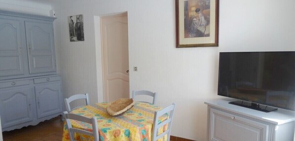 Una habitación con una mesa de comedor, sillas, televisor y un armario.