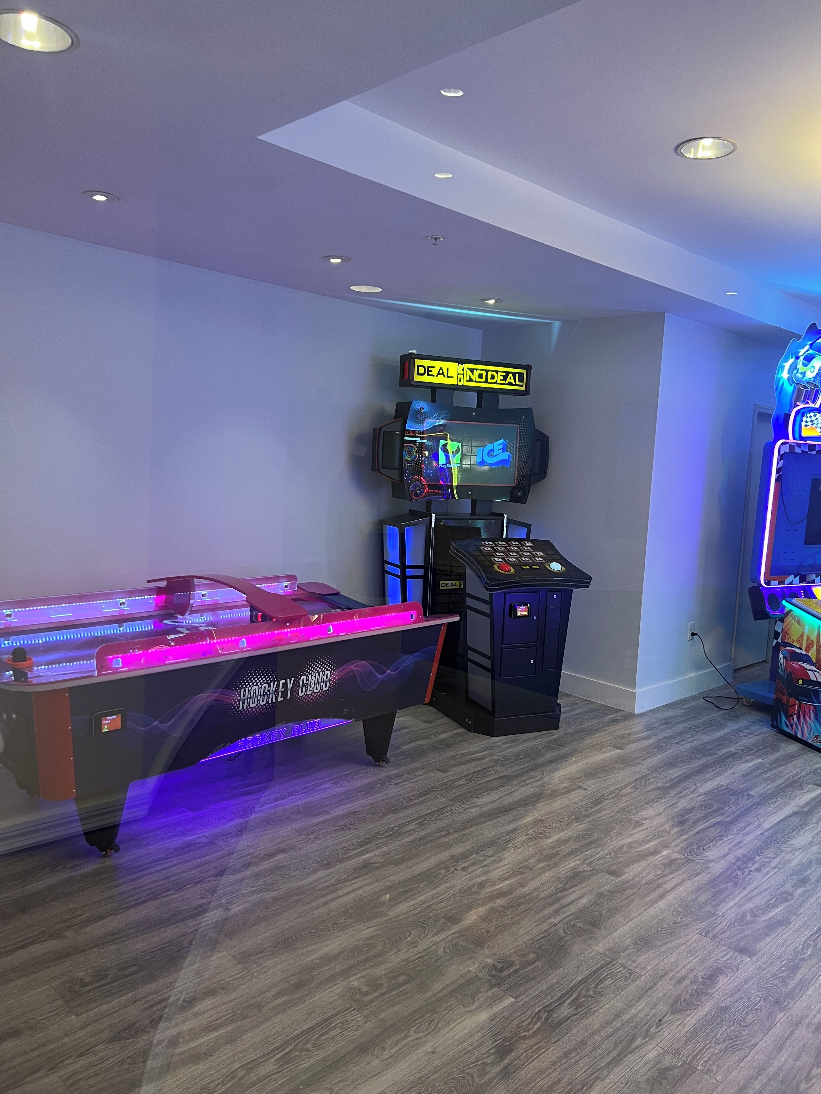 A room with a pool table, arcade machines, and a neon sign.