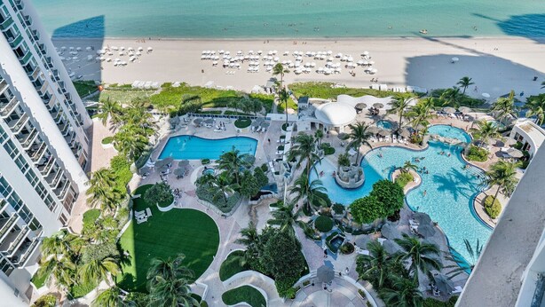 Un resort con varias piscinas, una playa y un edificio de gran altura.