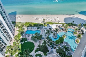 Ein Resort mit mehreren Schwimmbecken, einem Strand und einem Hochhaus.