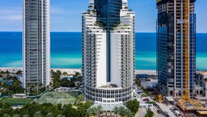 Un hotel moderno con fachada curva, varios balcones y vistas a la playa y al océano.