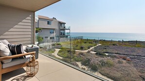 A balcony with a sofa and a wicker basket, overlooking a coastal landscape with a house and a clear sky. - High End Oceanfront Home, a 2 min walk to Beach, Shops, Dining & More in Solana (Solana Beach)