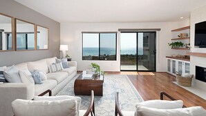 A modern living room with a large window, a sofa, a coffee table, and a fireplace. - High End Oceanfront Home, a 2 min walk to Beach, Shops, Dining & More in Solana (Solana Beach)