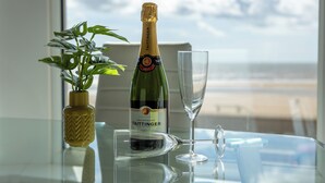 A bottle of Taittinger champagne, a glass, and a potted plant on a table with a view of the beach. - Highcliffe Seaview Suite (Blackpool)