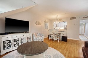 A modern living room with a flat-screen TV, a dining area with a round table, and a kitchen in the background. - LakeViews-Quaint/Quiet-Wlk 2 Beach-Kingston Plantation-Gated Community (Myrtle Beach)