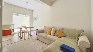 En moderne stue med en beige sofa, en grøn sofa og et spiseområde med et hvidt bord og stole.