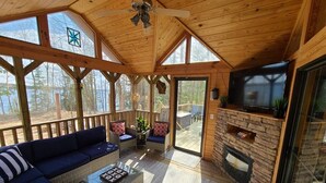 Uma cabana de madeira aconchegante, com um sofá grande, lareira e televisão.