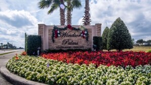 Une enseigne indiquant l’entrée de Windsor Palms, un complexe résidentiel de luxe avec accès contrôlé, agrémentée d’une composition florale devant.