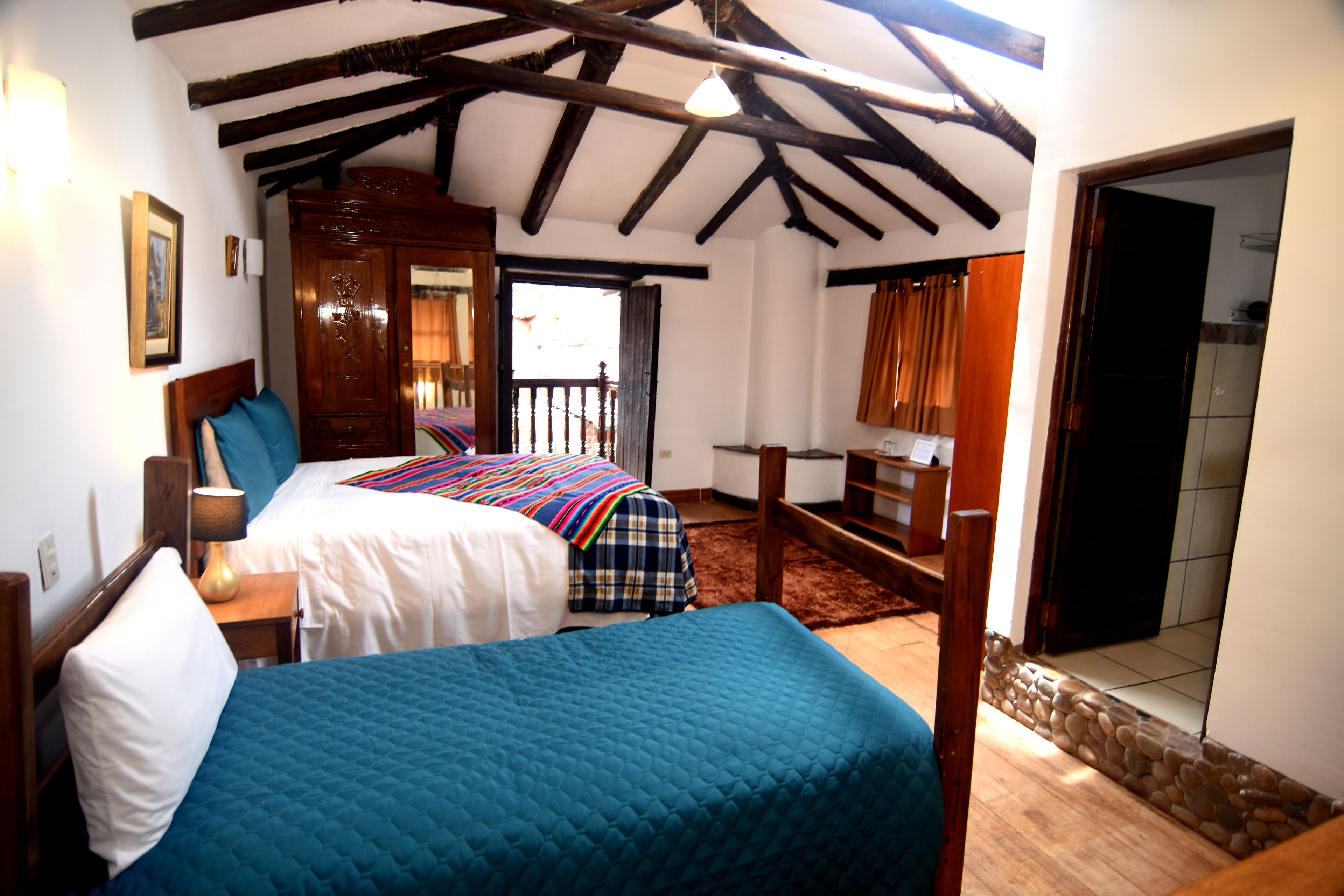 A bedroom with two beds, wooden beams on the ceiling, a wooden desk, and a stone wall.