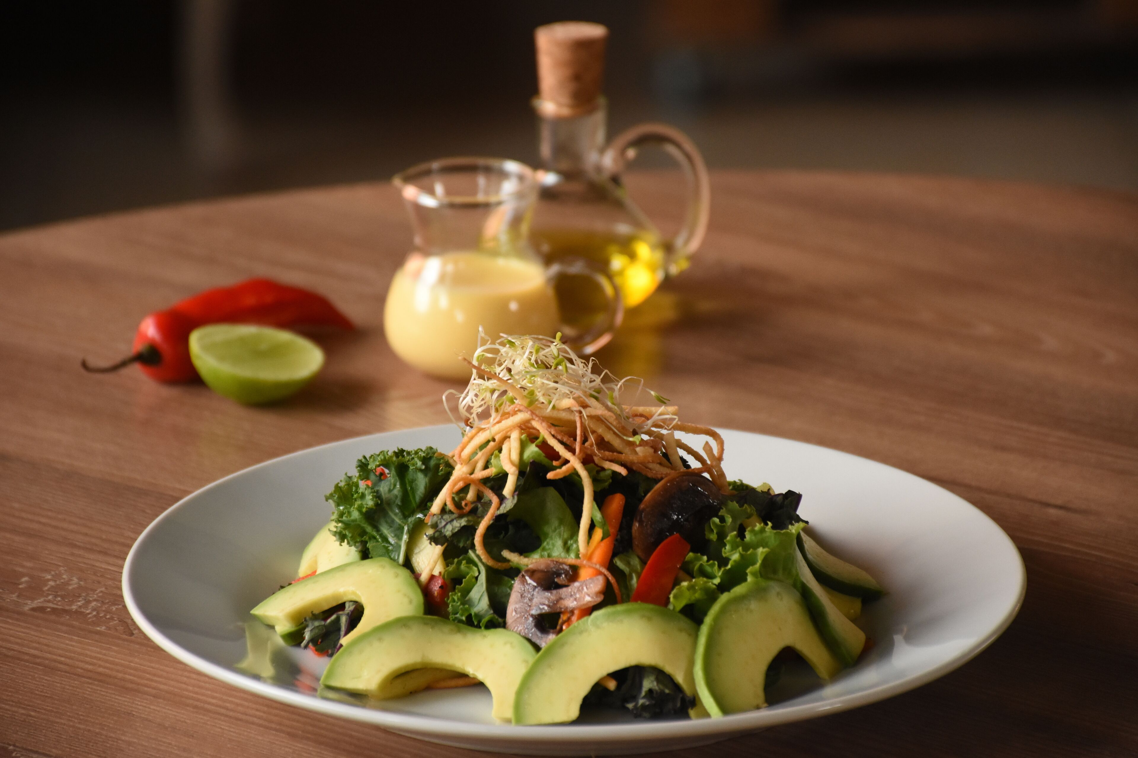A plate of salad with avocado, sprouts, and vegetables on a wooden table.