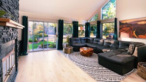A modern living room with a black leather sectional sofa, a patterned rug, and a stone wall.