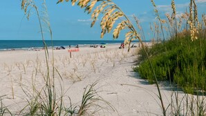 A beach with sand, grass, and a clear sky. - Ocean View! 100 steps to feet in the sand! Super Clean! (Jacksonville Beach)