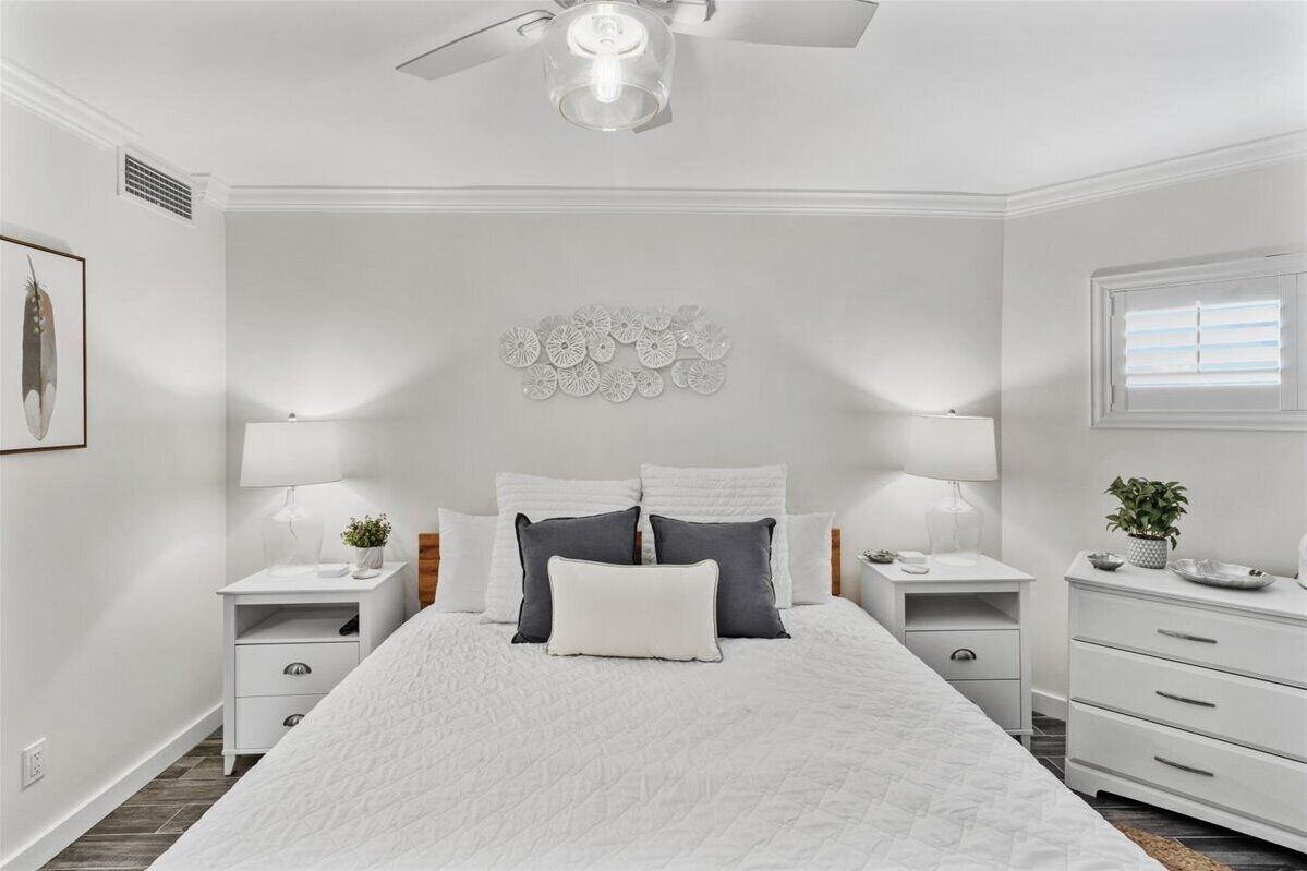 Een slaapkamer met een groot bed, twee nachtkastjes, een plafondventilator en een raam met zonwering.