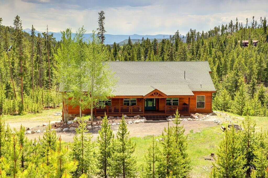 A cabin with a wooden exterior, a porch, and a view of a forested mountain range.