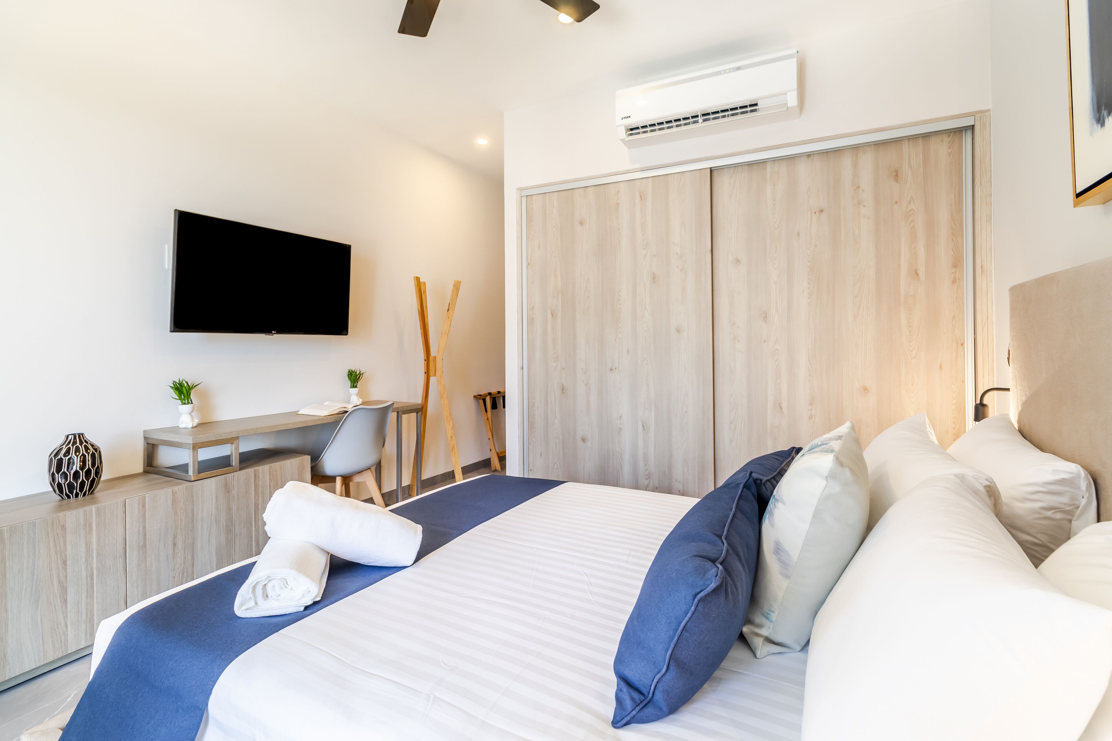 Ein modernes Hotelzimmer mit einem großen Bett, einem Schreibtisch mit Stuhl, einem Flachbildfernseher und einem Holzschrank.