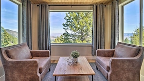 Une pièce avec un plafond en bois, deux fauteuils en cuir marron, une table basse en bois et une vue sur les arbres et les collines, visible à travers de grandes fenêtres.