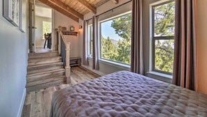 Une chambre avec un grand lit, un escalier en bois et de grandes fenêtres donnant sur la forêt.