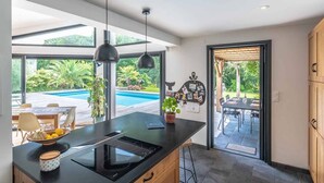 A modern kitchen with a large island, black appliances, and a view of a swimming pool and garden.