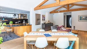 A modern kitchen with wooden beams, a dining area with a large table and chairs, and a cozy living space with a sofa and a painting.