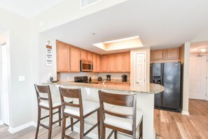 A modern kitchen with wooden cabinets, a granite countertop, and a stainless steel refrigerator. - 4th Floor condo at The Palms of Destin with Seasonal Beach Shuttle! (Destin)