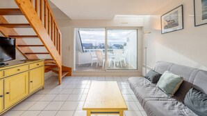 A living room with a wooden staircase, a sofa, a yellow cabinet, and a TV. - Carnac - 3-room apartment - 50m² - Pool (CARNAC)