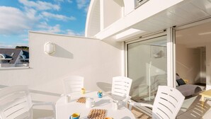 A modern outdoor patio with white furniture, a glass door leading to a room, and a clear sky. - Carnac - 3-room apartment - 50m² - Pool (CARNAC)