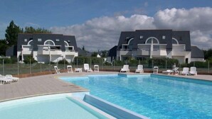 A swimming pool with lounge chairs and a building with a modern design in the background. - Carnac - 3-room apartment - 50m² - Pool (CARNAC)