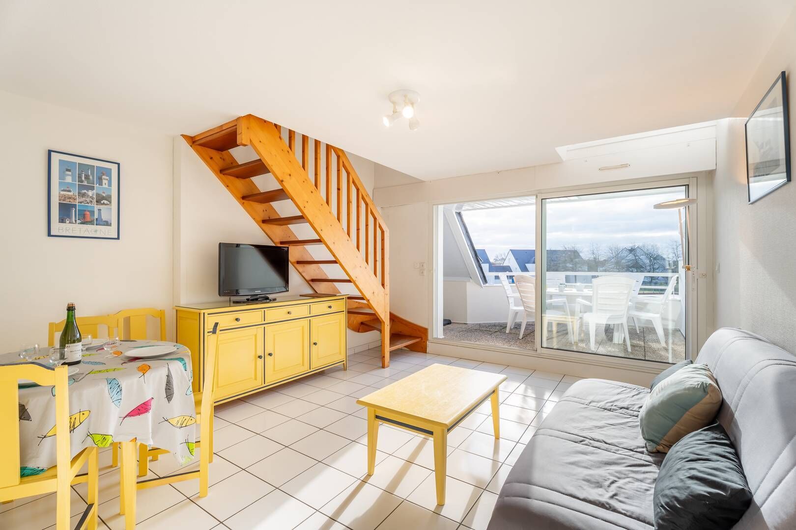 Una sala de estar moderna con una escalera de madera, un comedor y un balcón con vistas.