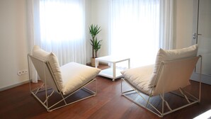 A room with two beige chairs, a small white table, and a potted plant.