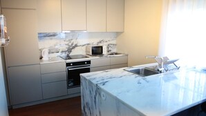 A modern kitchen with white cabinets, a marble countertop, a built-in oven, a microwave, and a sink.