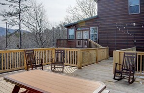 Une terrasse en bois avec une table et des chaises, une vue sur une montagne et un bâtiment doté d’un balcon.