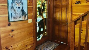 A wooden interior with a framed painting of a wolf, a glass door with a bear silhouette, and a wooden staircase.