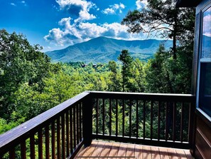 Una terraza de madera con vistas a una montaña y un bosque denso.