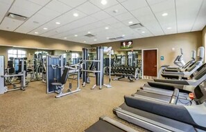 Une salle de sport équipée de divers appareils d’exercice, notamment des tapis de course, des appareils de musculation et des poids libres.