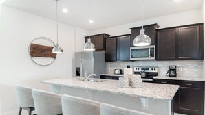 Una cocina moderna con armarios oscuros, encimera de granito, electrodomésticos de acero inoxidable y taburetes de bar.