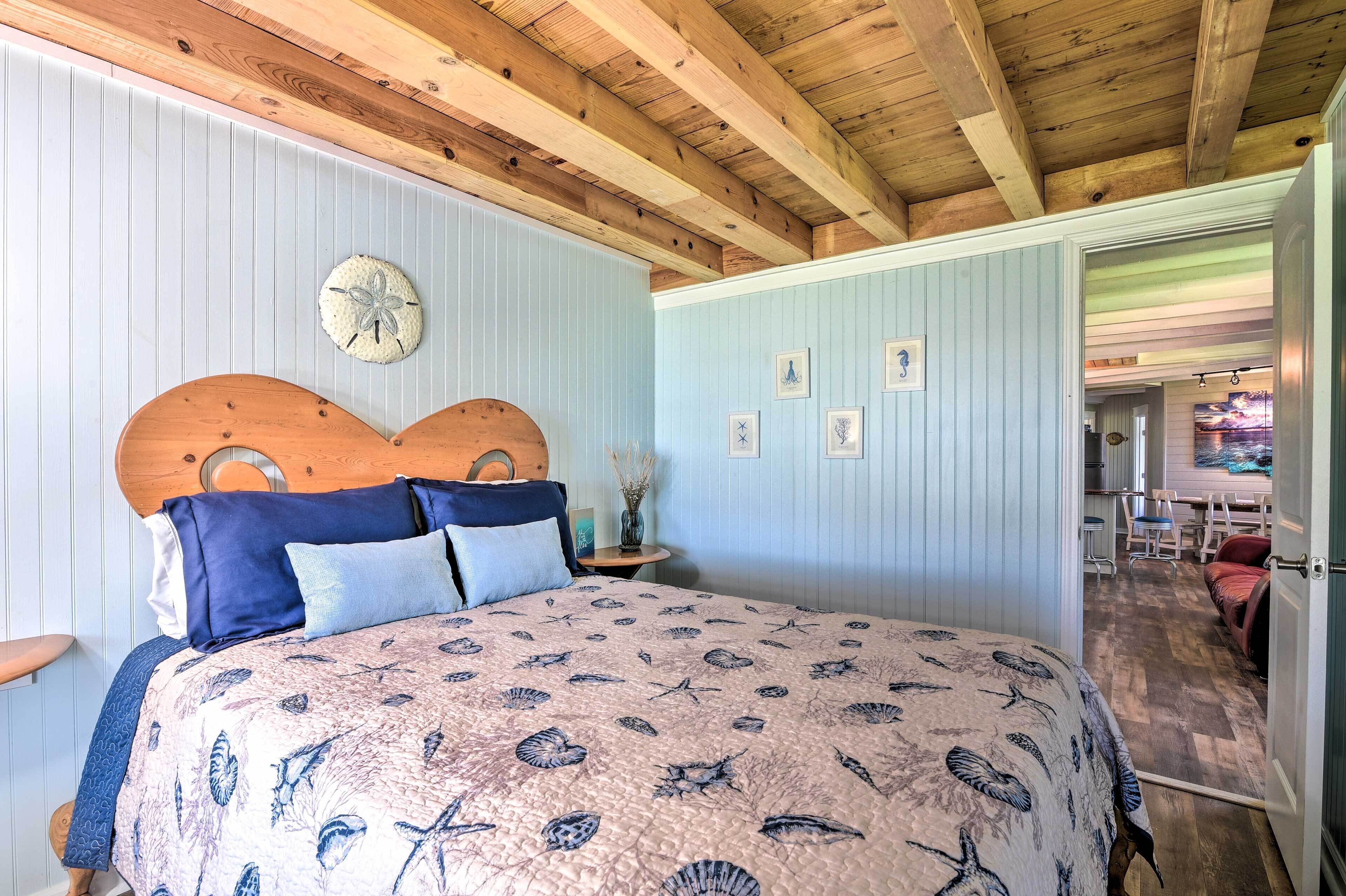 Un dormitorio con cabecera de madera, cama con colcha estampada, un reloj de pared redondo y una mesita de noche con un florero.