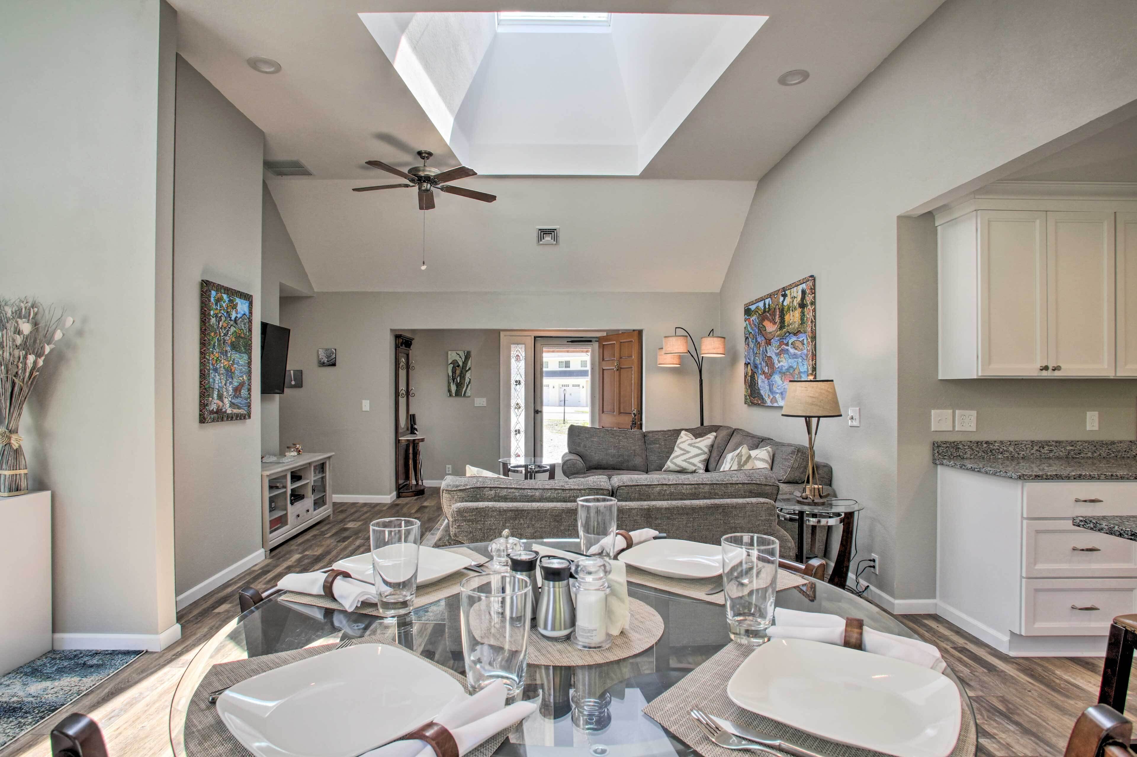 Un coin repas avec une table en verre, de l’assiette blanche et un ventilateur de plafond.