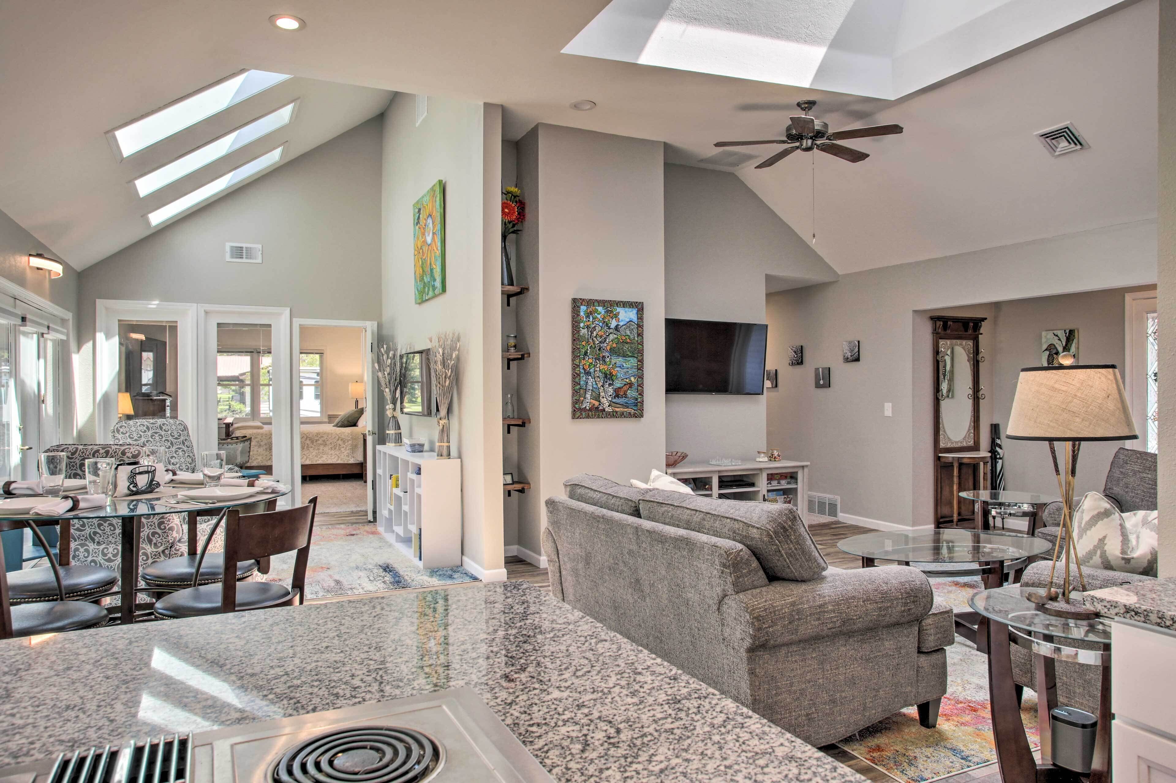 A spacious living area with a high ceiling, skylights, a ceiling fan, and a large flat-screen TV.