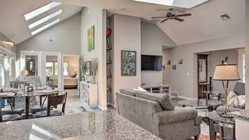 A spacious living area with a high ceiling, skylights, a ceiling fan, and a large flat-screen TV.