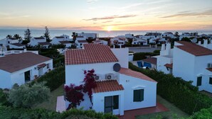 Un quartier résidentiel en bord de mer, avec des maisons blanches et des toits recouverts de tuiles rouges, entouré de verdure et offrant une vue sur la mer.