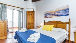 Une chambre à coucher avec un lit, un tableau représentant un coucher de soleil, une tête de lit en bois et une couverture bleue.