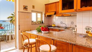 A kitchen with wooden cabinets, a granite countertop, and a view of the ocean. - La Casa di Elvira - Sea View (Giardini Naxos)