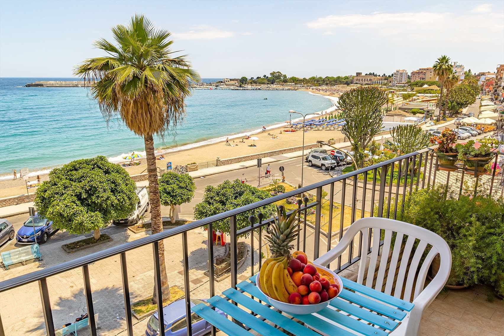 Un balcón con vista a la playa, un frutero y una silla azul.
