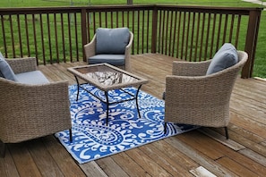 A deck with wicker furniture, a glass-top table, and a blue patterned rug.