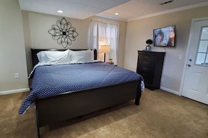 A bedroom with a bed, a wall-mounted decorative piece, a television, and a door.