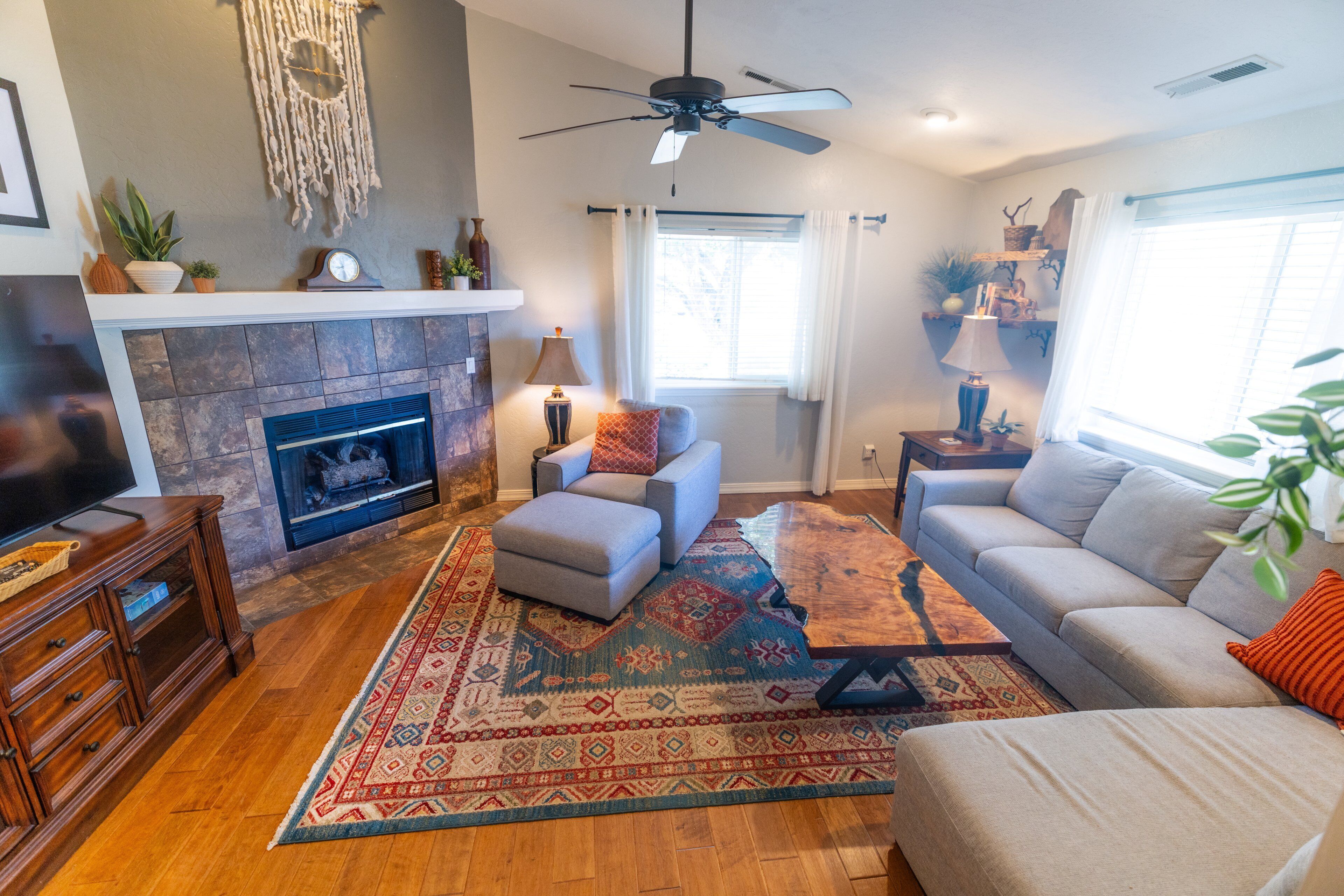 A living room with a fireplace, a ceiling fan, and a large window.